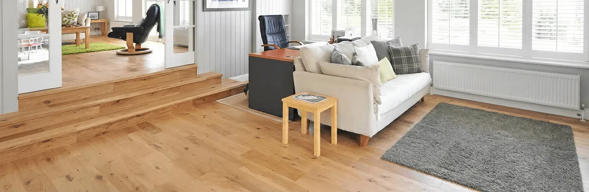 A modern living room with professionally installed laminate flooring, a beige sofa, a small side table, a gray rug, and large windows with white shutters in Columbus, OH